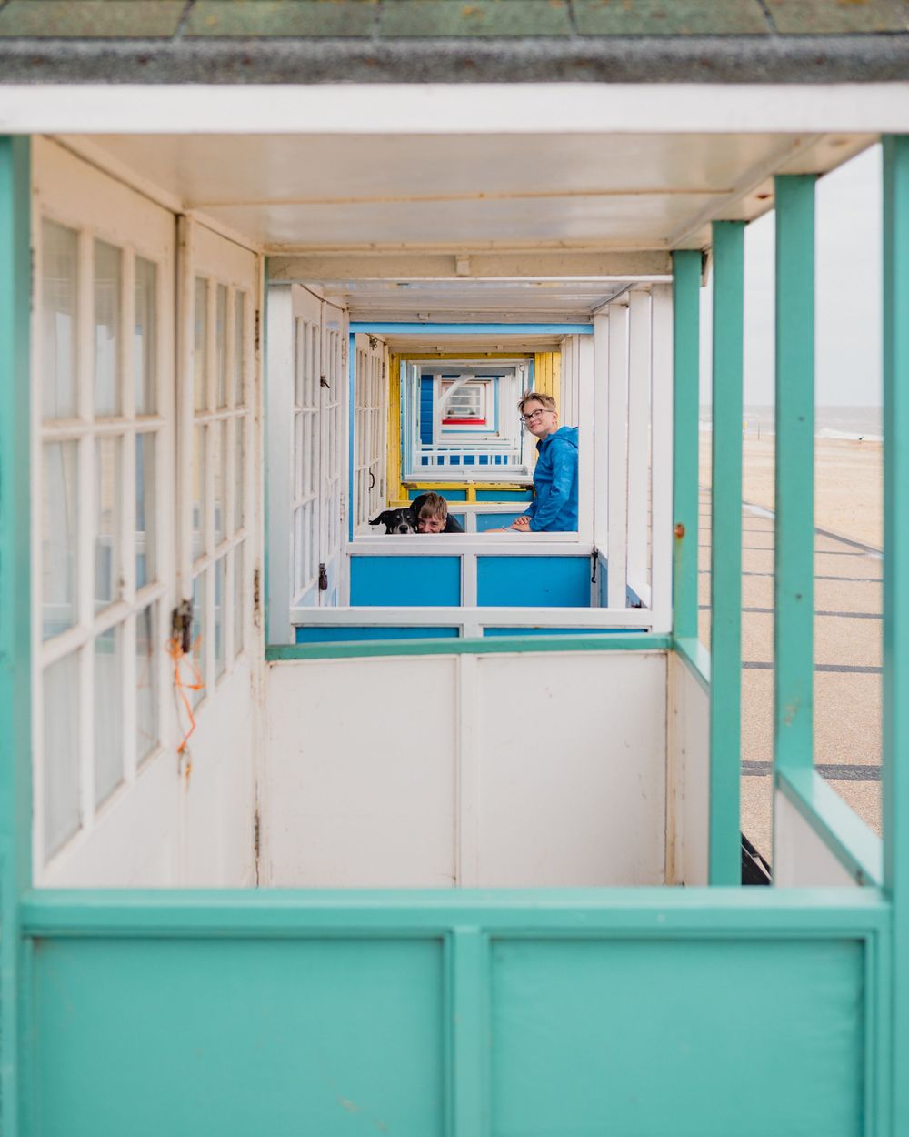 A pastel-coloured beach hut corridor with mint green and white panels leads to a distant ocean view.