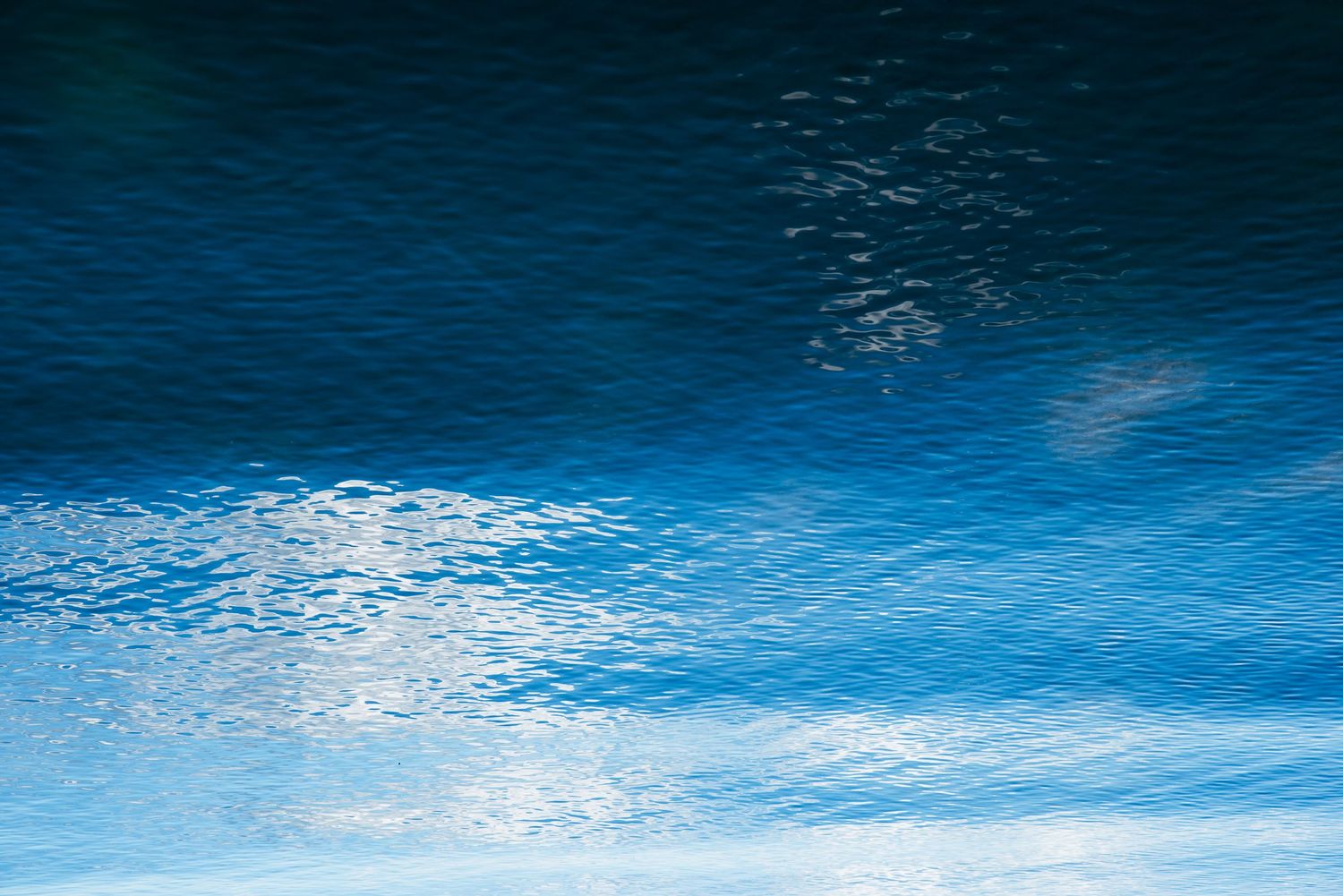 Abstract water reflection creates a mesmerizing pattern of blue tones and ripples against a dark background.