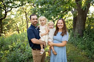 A family poses together outdoors in a wooded setting during golden hour.  Kendall Kuss Photography Watertown WI