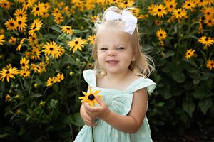 A toddler in a mint green dress explores a garden filled with bright yellow black-eyed susan flowers in summer.  Kendall Kuss Photography