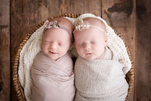 Two sleeping newborn babies swaddled in light fabric lying together in a woven basket with white blanket.  Kendall Kuss Photography