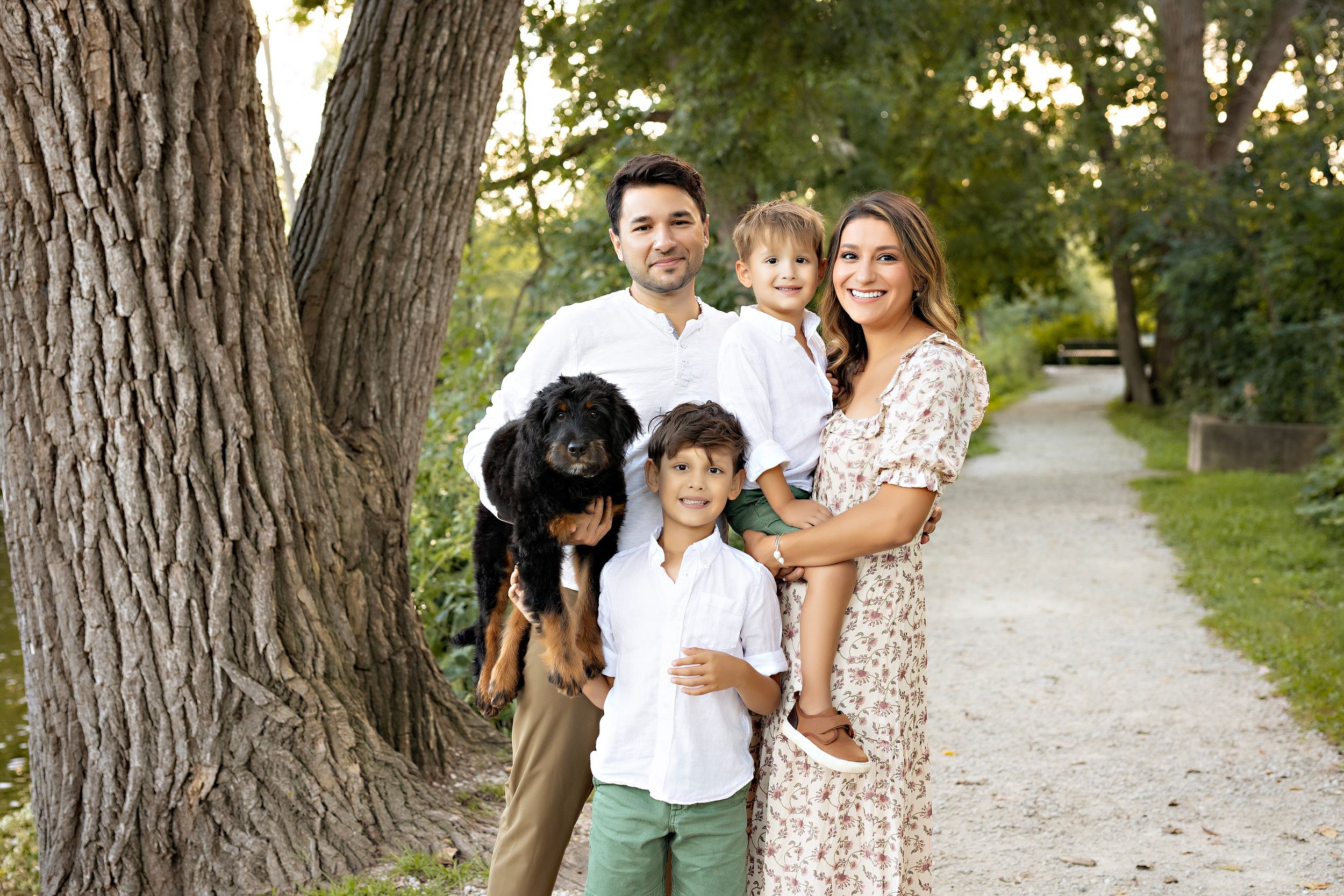 Family and dog walking together on a tree-lined gravel path on a sunny summer day. Delafield WI family photographer