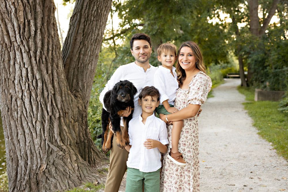 Family and dog walking together on a tree-lined gravel path on a sunny summer day. Delafield WI family photographer