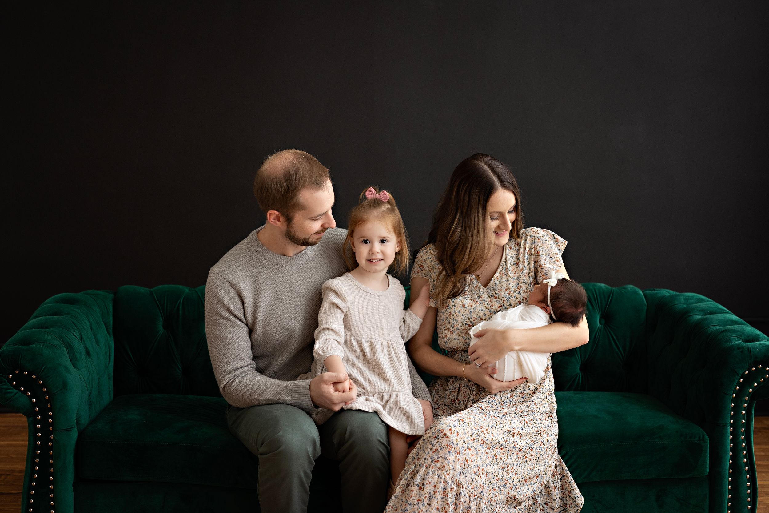 Intimate family portrait on emerald green velvet sofa against dark backdrop. Family photography by Kendall Kuss in Watertown WI
