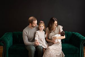 Intimate family portrait on emerald green velvet sofa against dark backdrop. Family photography by Kendall Kuss in Watertown WI