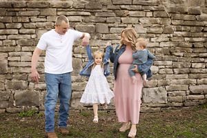 A family pose playfully in front of a rustic stone wall for a casual outdoor photo session.  Kendall Kuss Photography Watertown WI