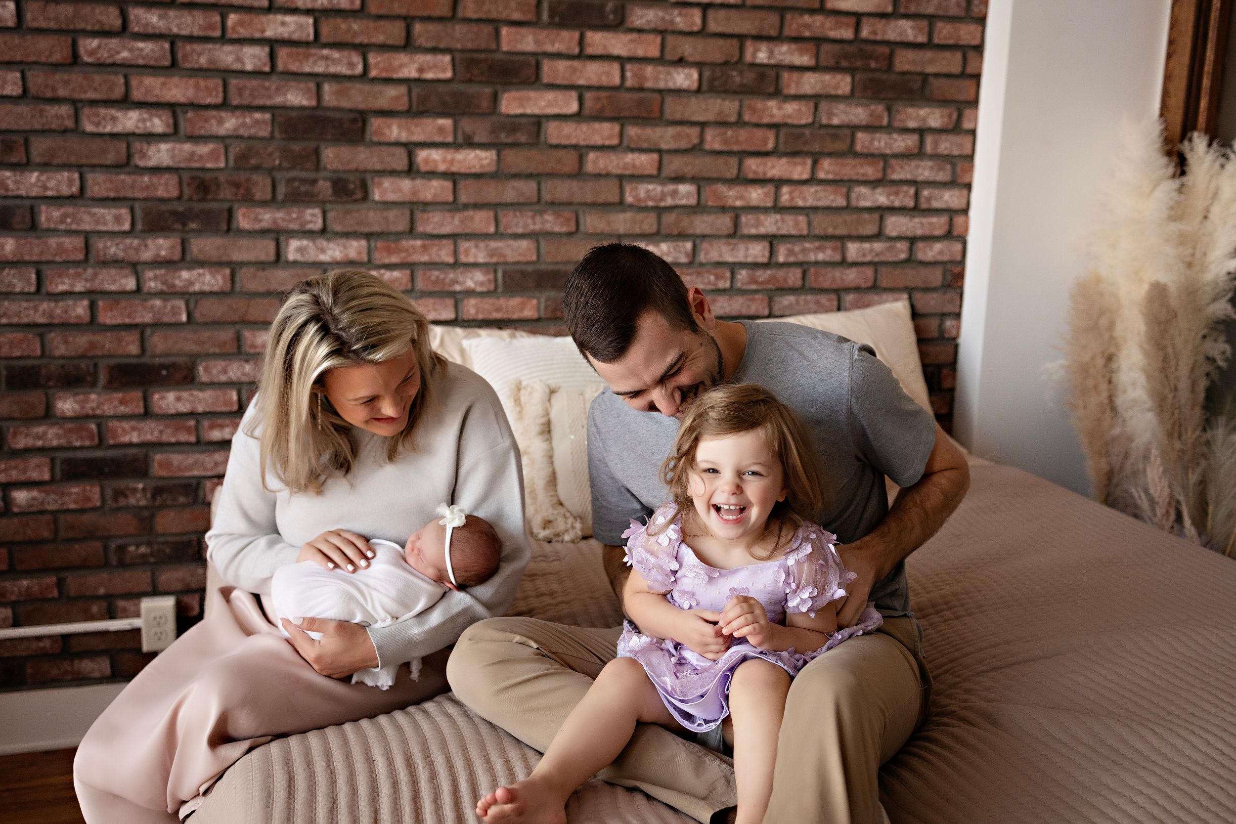 Casual family moment on beige couch against brick wall backdrop. Lifestyle newborn photography at Kendall Kuss Photo studio in Watertown WI