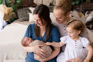 A family sits together on a bed, sharing a tender moment with their newborn baby while smiling warmly.