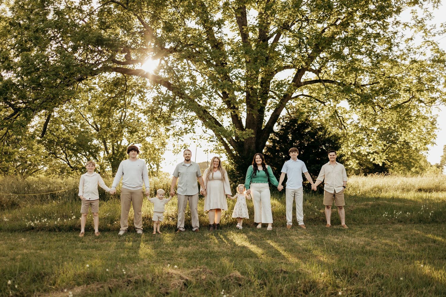 A group in white outfits poses together on a grassy hillside at sunset.