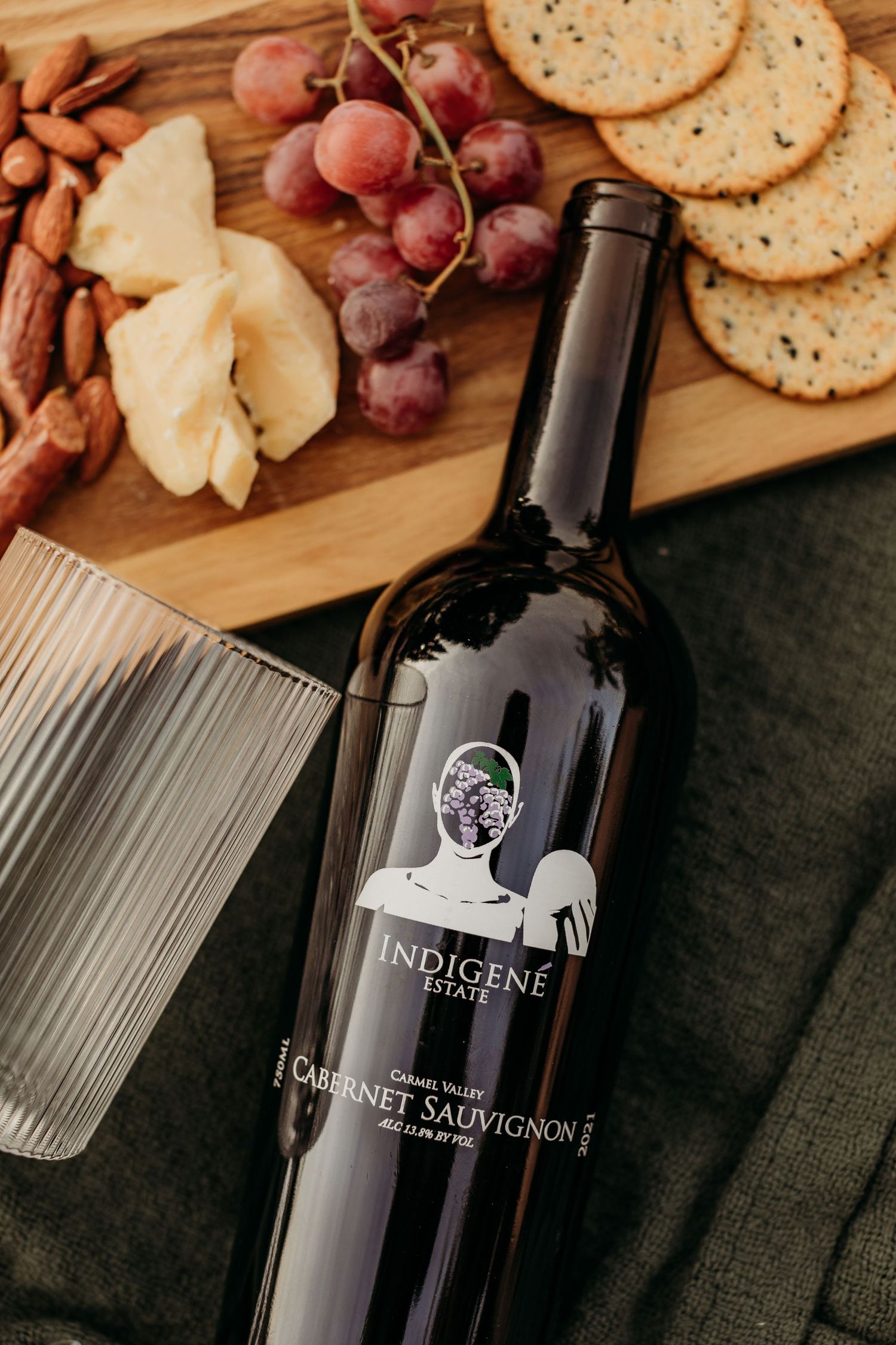 Wine bottle laying next to charcuterie board with cheese, crackers, and grapes.