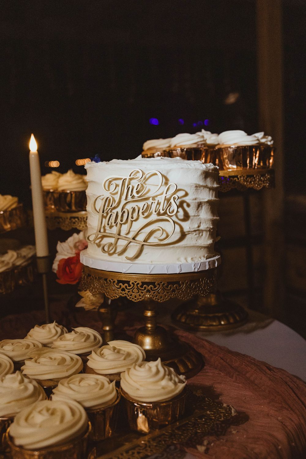 Wedding cake display featuring white frosted cupcakes and decorative name signs in elegant gold lettering.