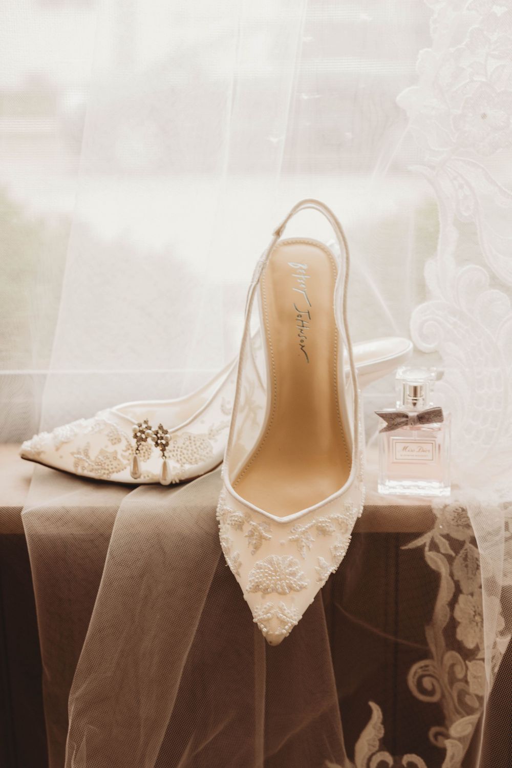 Elegant bridal shoes and perfume bottle arranged with delicate lace veil details.