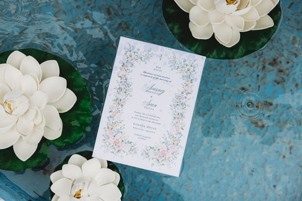 Elegant floral wedding invitation displayed beside white magnolia flowers on a blue surface.