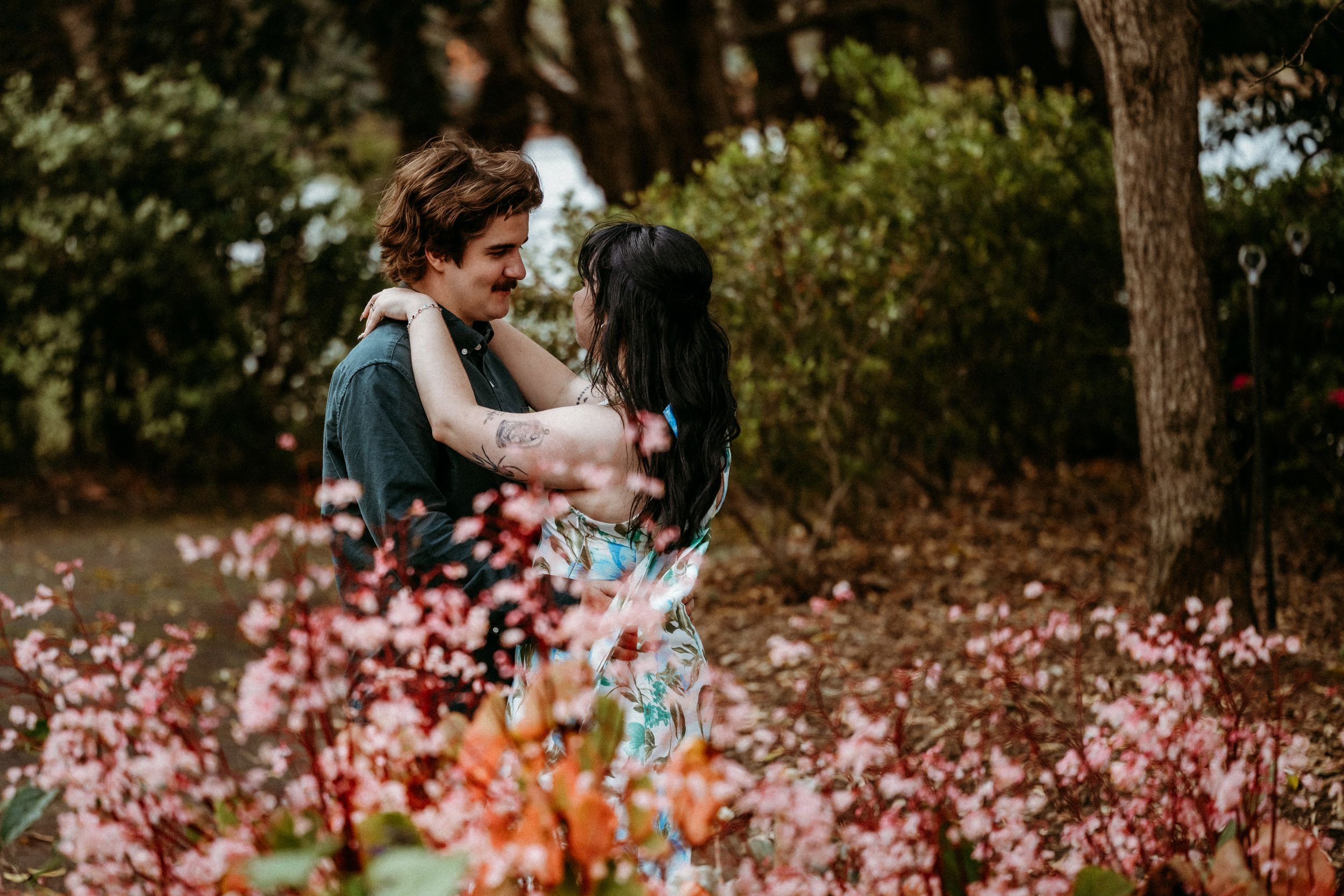 A couple embraces in a garden filled with pink and orange cosmos flowers on a sunny autumn day.