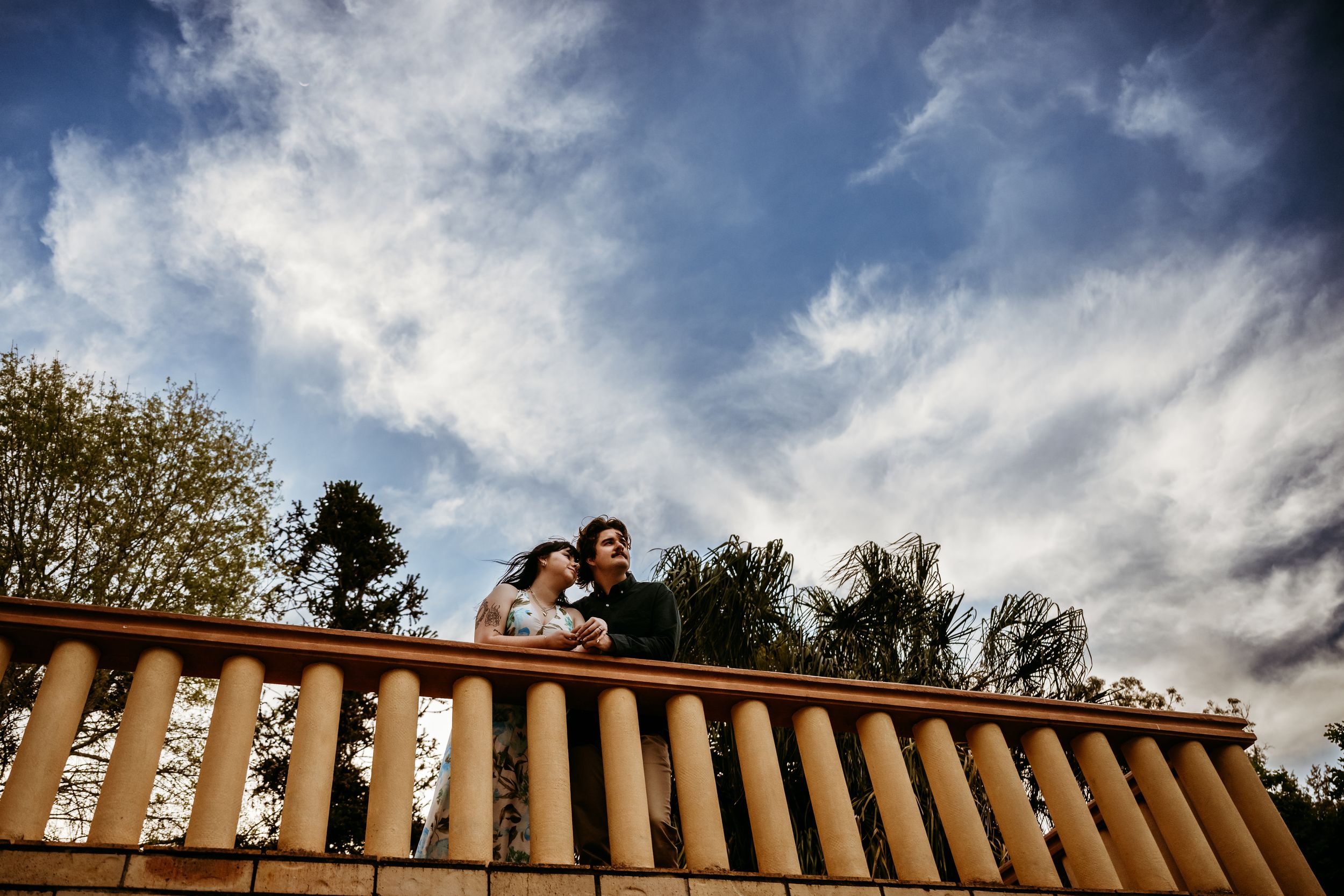 Dramatic panoramic view of a stone balustrade against cloudy sky with trees silhouetted in the background.
