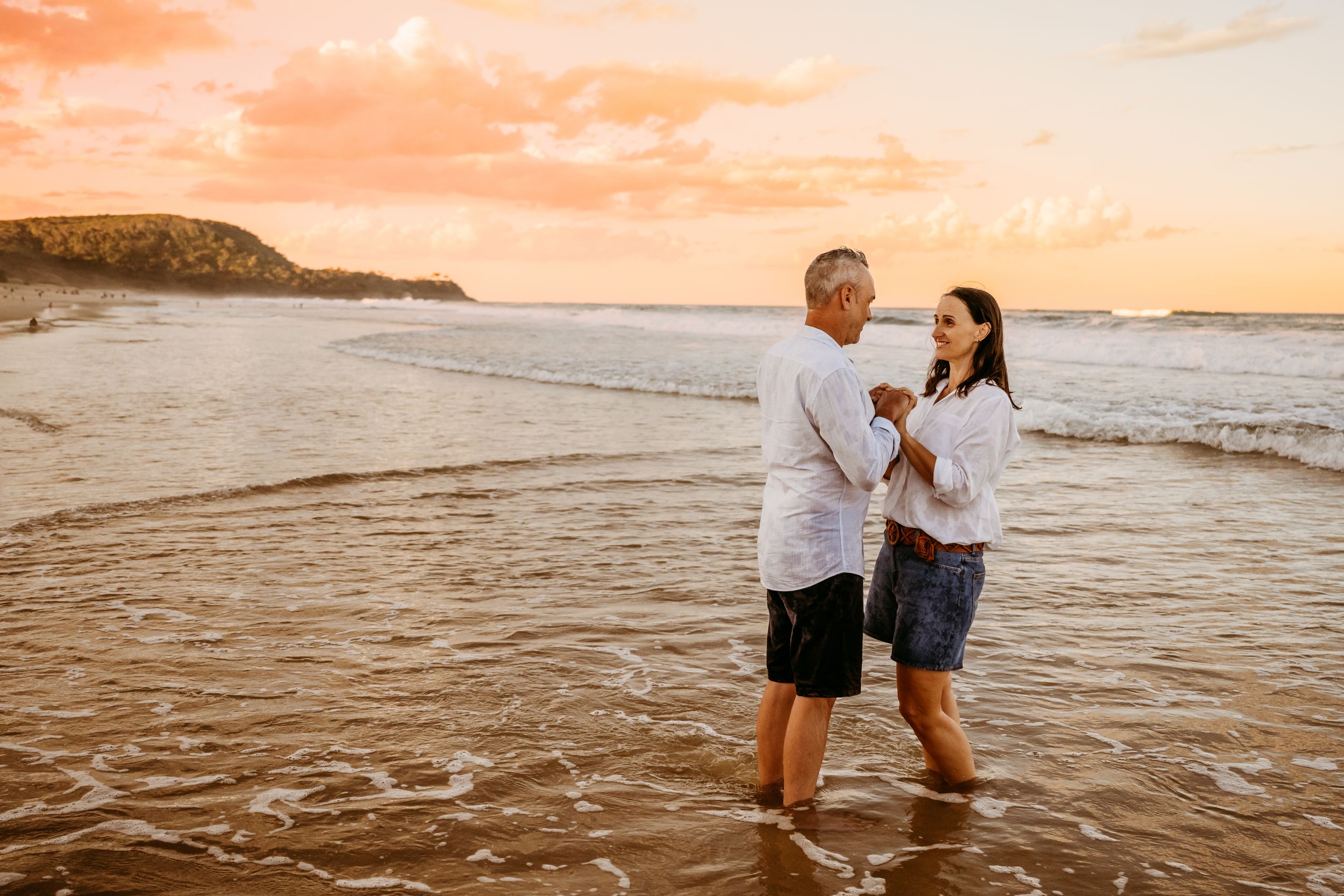 A couple shares a romantic moment at the beach during golden hour as waves lap at their feet.