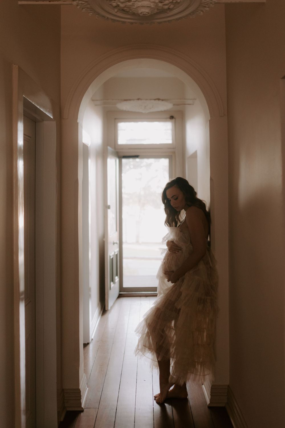 Moody indoor portrait in a long hallway with arched windows and natural light.