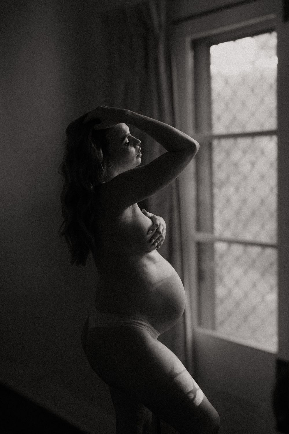 Black and white window portrait with dramatic shadows and natural light.