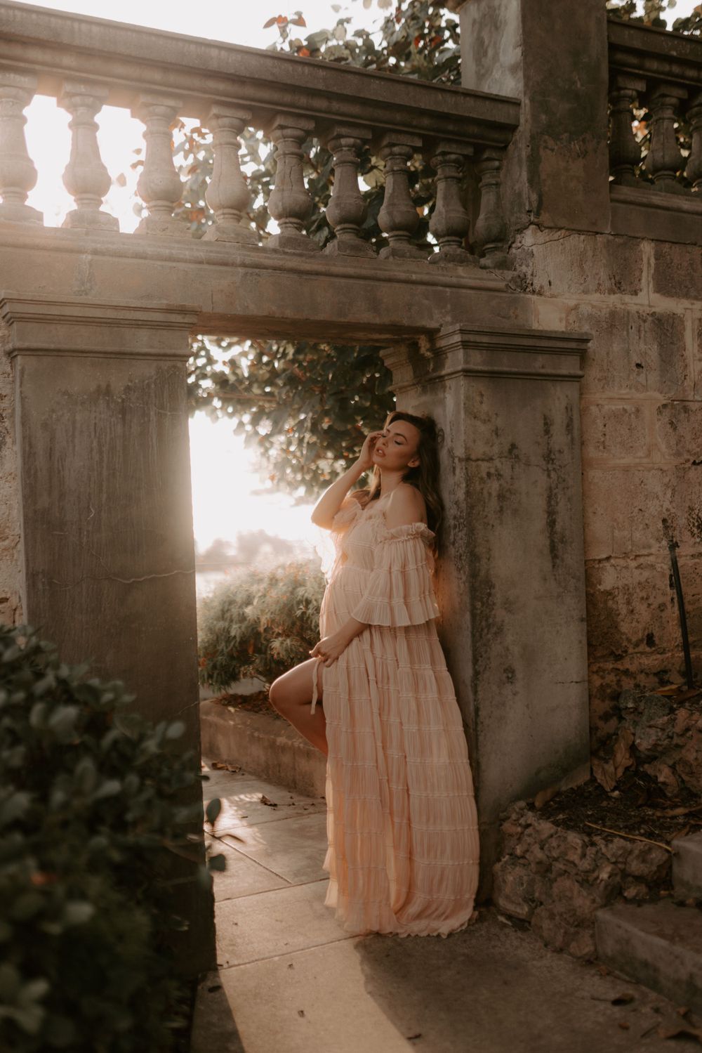 A maternity photo session featuring a woman in a vintage-style dress among stone columns.