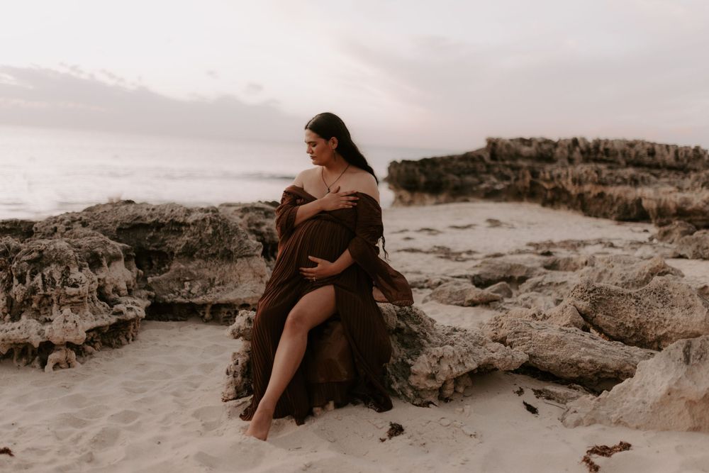 Couple embracing on rocky beach at sunset with dramatic coastal landscape.