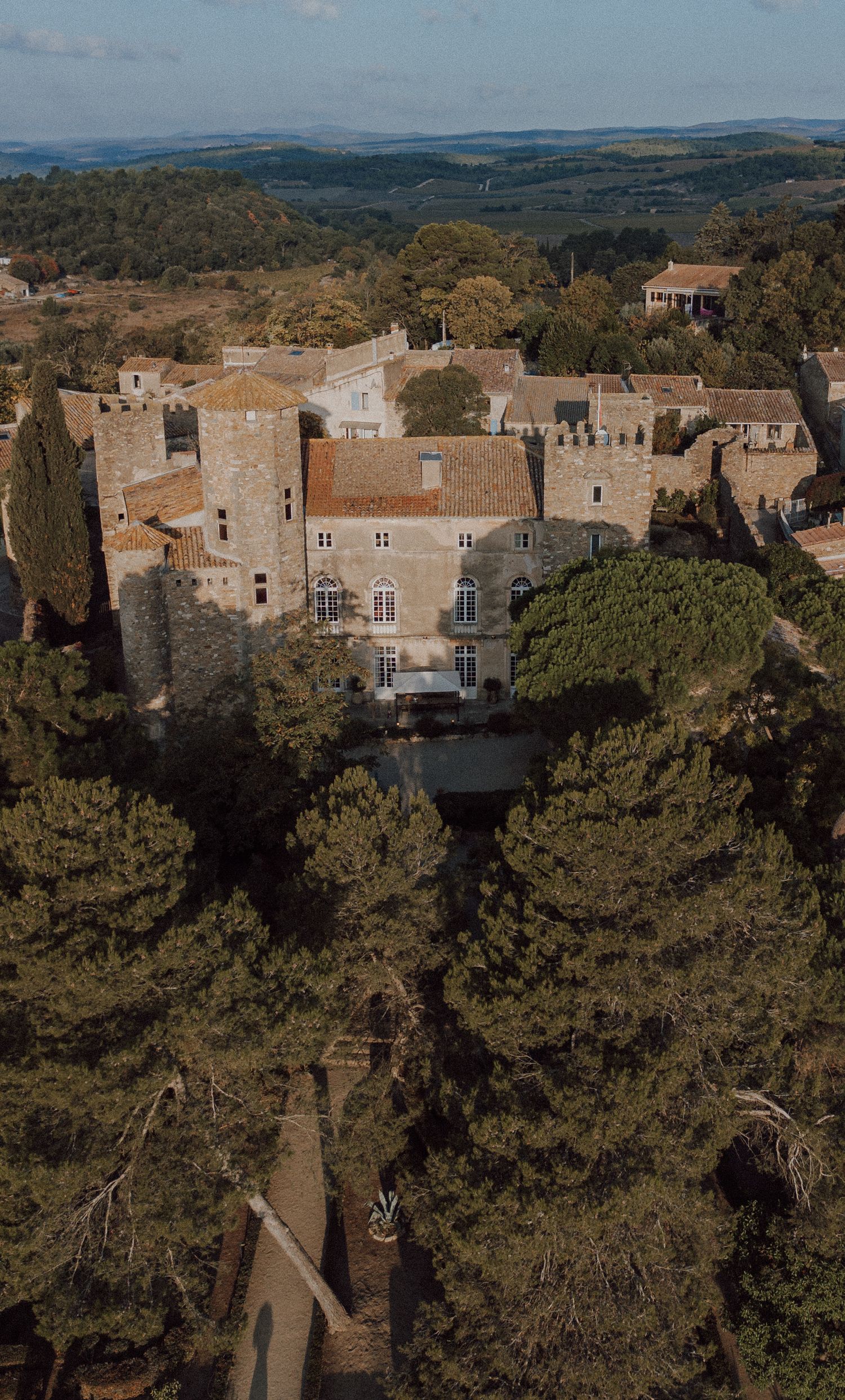 Aerial view of a historic stone castle with towers surrounded by cypress trees in the French countryside.