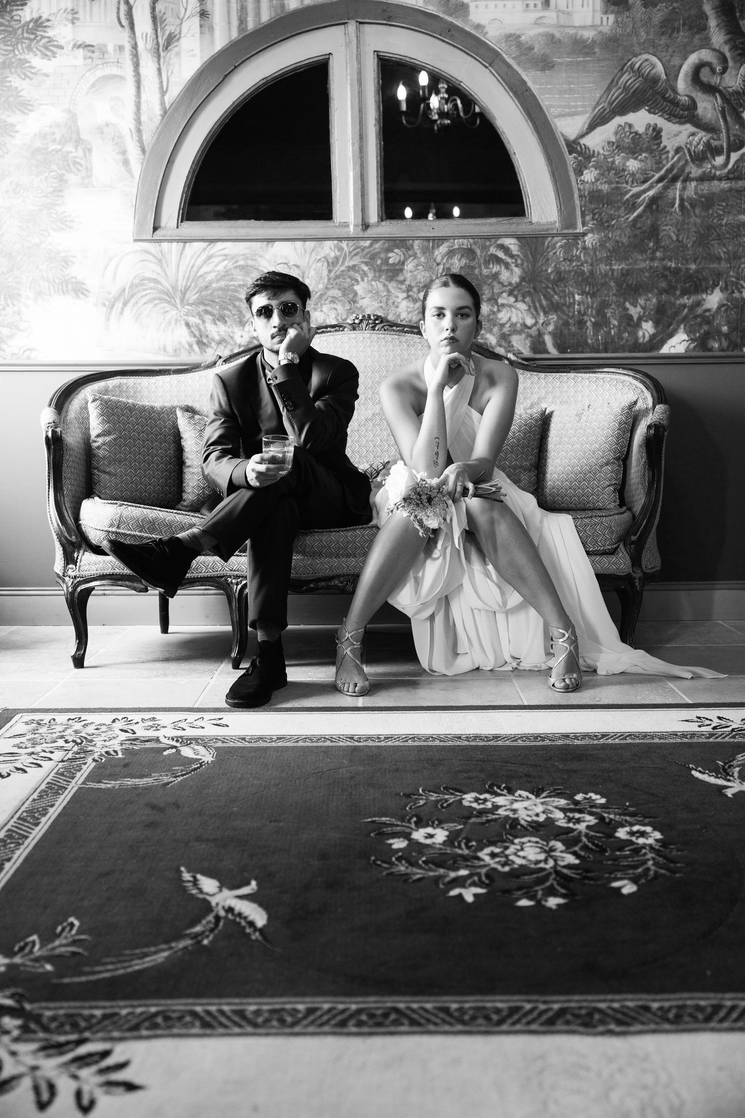 Black and white wedding photos showing couple lounging on ornate rug in vintage-style setting.