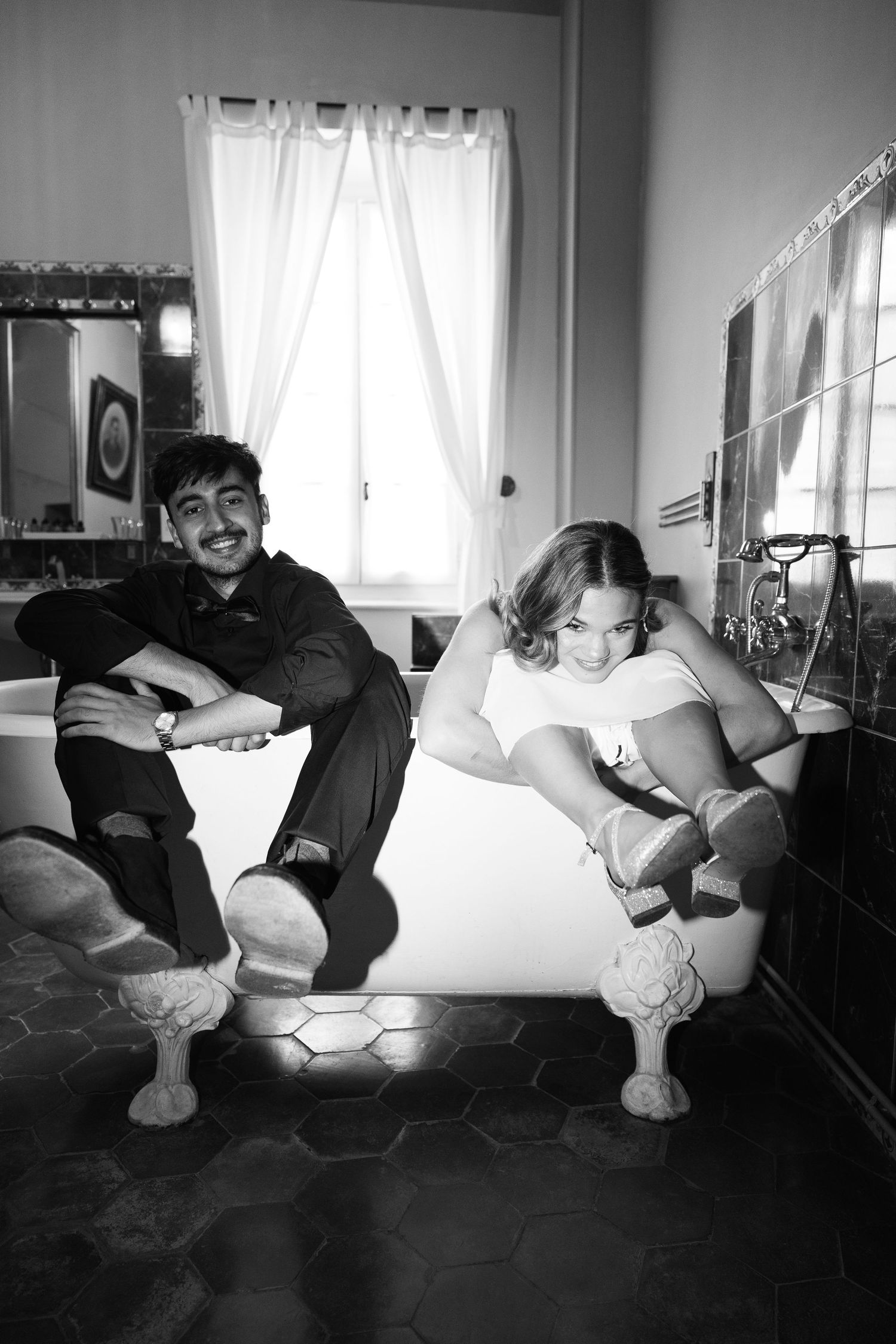 Two people sitting and laughing together on a tiled floor by a bright window.