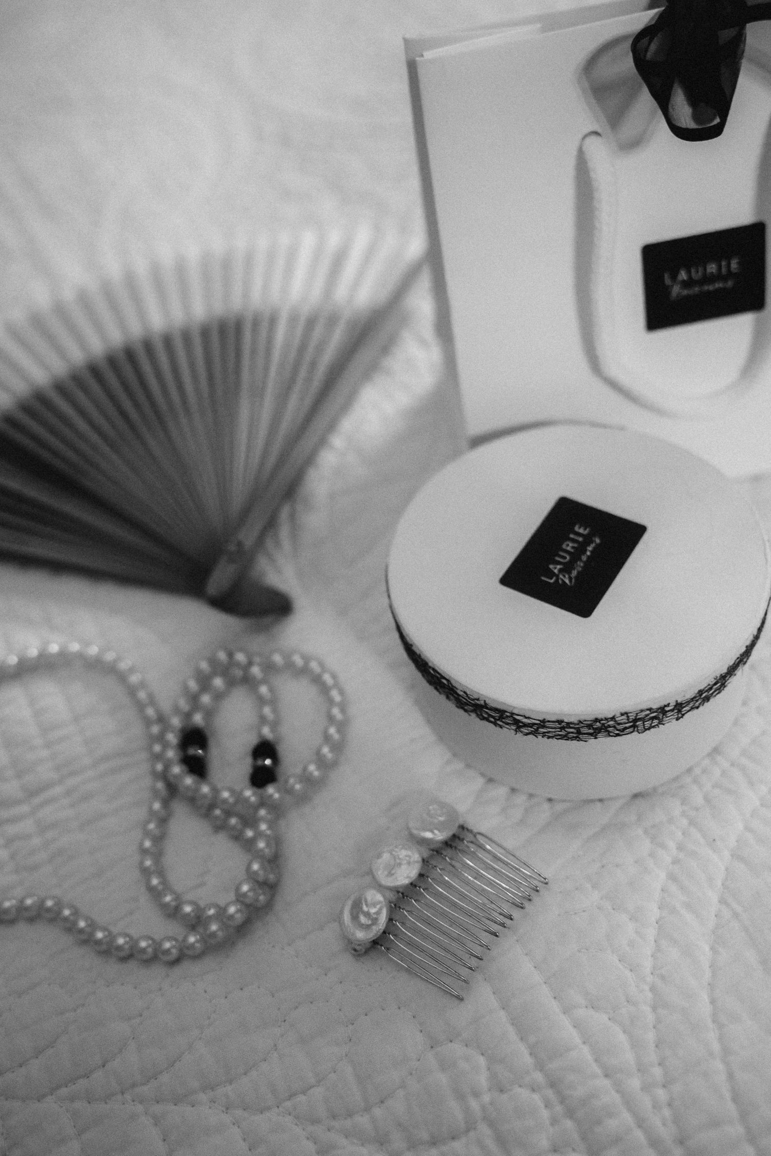 Wedding accessories including pearl necklace, hair comb and decorative fan arranged on white textured surface.