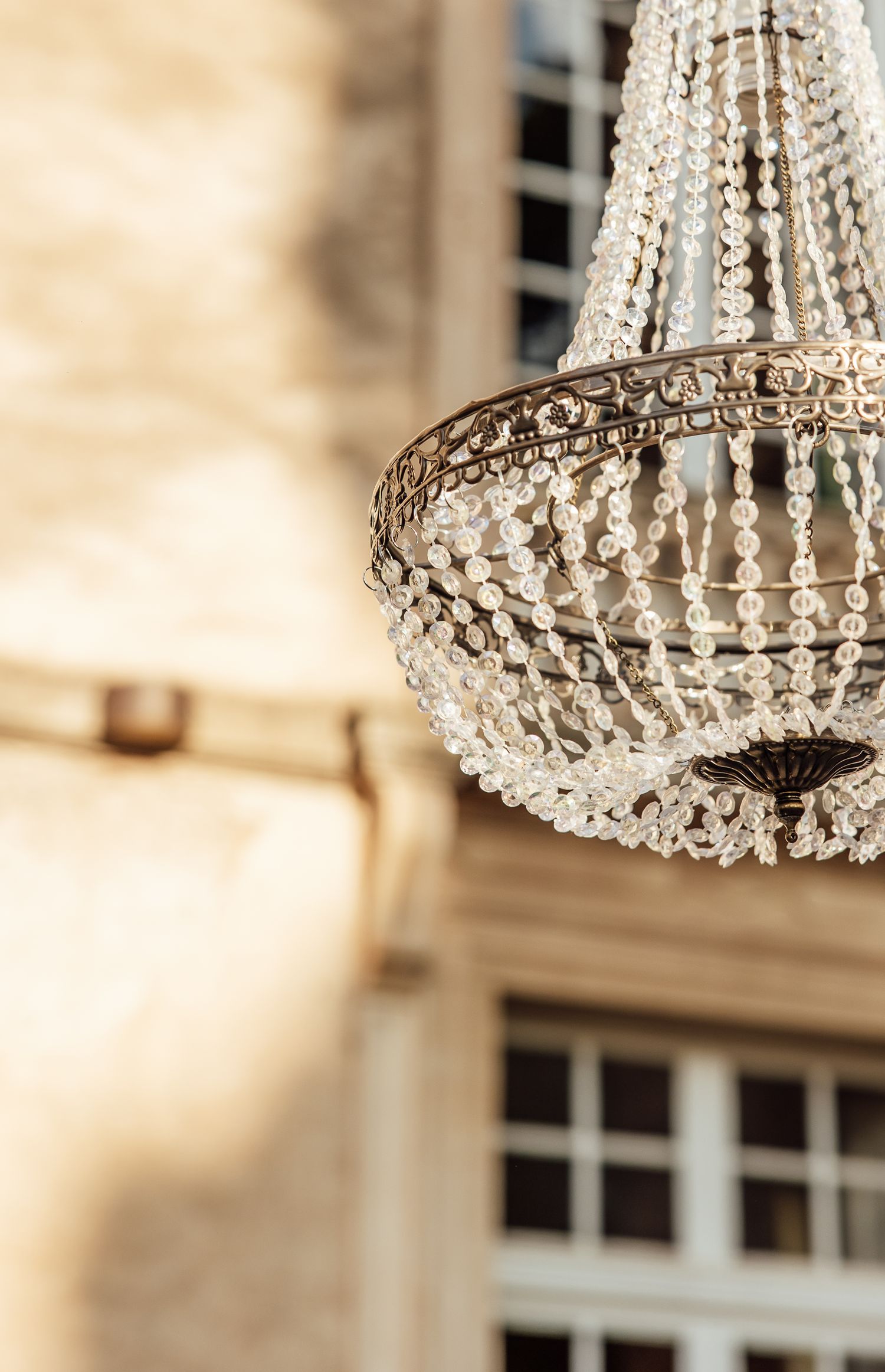 Crystal chandelier with hanging glass prisms creates elegant lighting against a soft beige interior background.