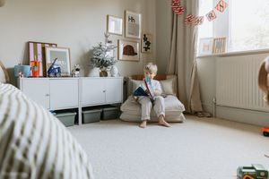 Child sitting in playroom with white storage furniture and natural decor.