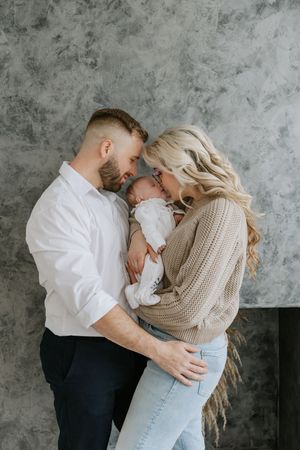 An intimate family moment against a textured grey wall background.