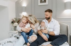 A family moment captured on a bed with grey bedding and white paneled walls.