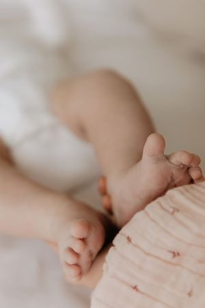 Close-up view of tiny baby feet against soft pink blanket showing delicate toes and skin texture.