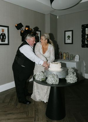 A couple cuts their wedding cake together during their reception in a dimly lit room.