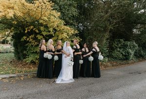 Wedding party poses together in autumn setting with black bridesmaid dresses and white decor.