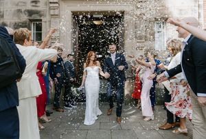 Wedding guests throw confetti at the newlyweds outside a stone building during a joyous celebration.