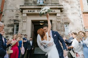 Wedding guests celebrate and toss confetti outside a historic stone building entrance during a joyful ceremony exit.