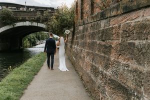 Couple walks along a scenic stone wall path surrounded by lush greenery on their wedding day.