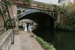 A scenic view of an old brick canal bridge and towpath with stone walls and overhanging trees in autumn.