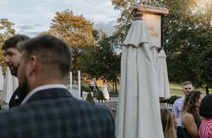A wedding reception table setup outdoors with white umbrellas and string lights at sunset.