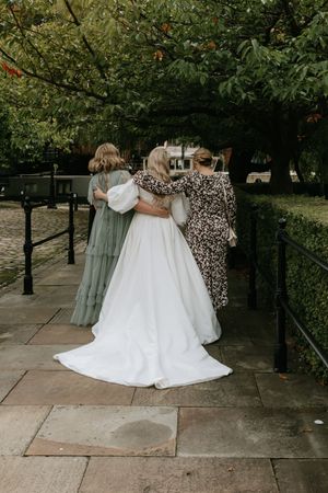 A wedding party walks down a tree-lined path on a sunny afternoon.