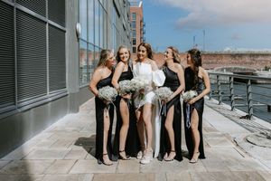 Wedding party wearing black and white formal attire poses together showing their shoes on urban steps.