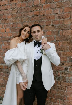 A couple in wedding attire poses playfully against a rustic brick wall in three candid shots.