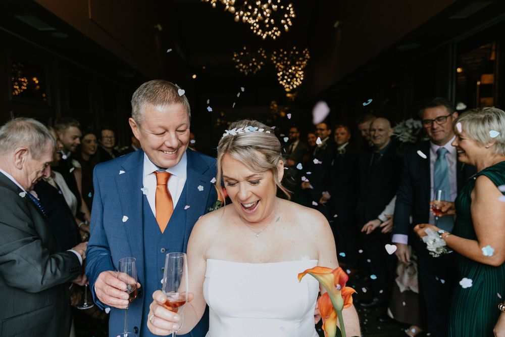 Wedding guests laugh and dance together on a dimly lit dance floor under glowing string lights during reception celebration.