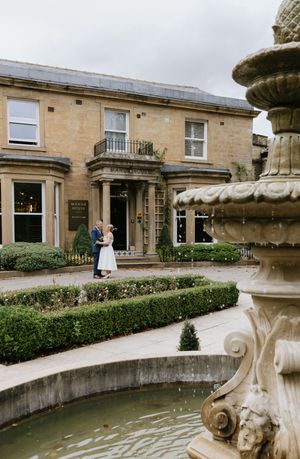 Elegant stone building exterior with manicured hedges and decorative fountain feature creates a sophisticated wedding venue setting.