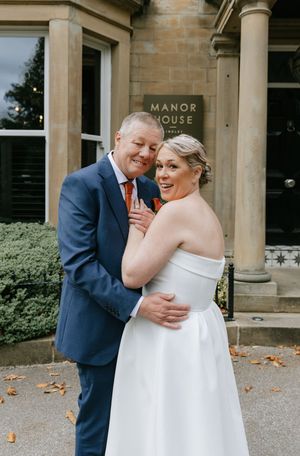 A joyful couple shares a tender moment in front of a stately manor house on their wedding day.