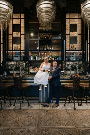 A couple in formal attire shares intimate moments at an elegant bar with industrial-chic decor and patterned flooring.