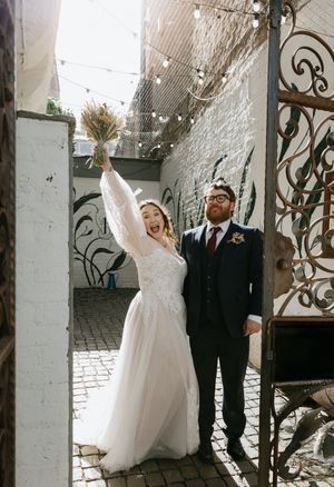 A couple celebrates their wedding day in an elegant indoor venue with white brick walls and decorative iron details.