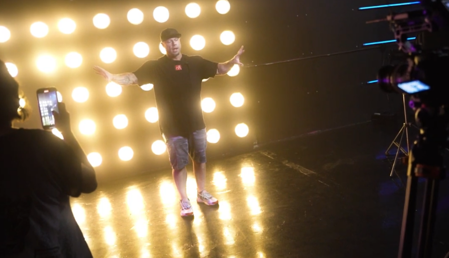 Person performing on stage with bright spotlight wall of glowing bulbs in background.