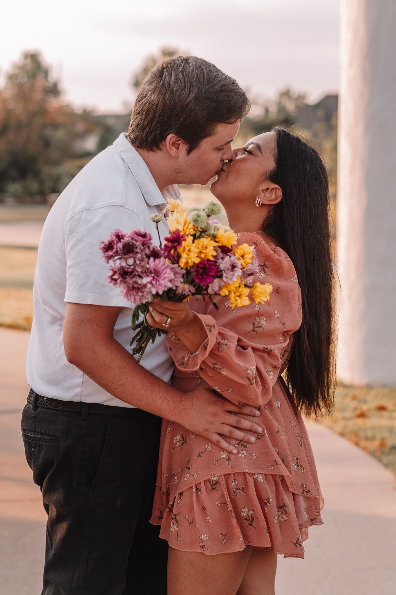 Romantic couple sharing a tender moment with colorful flowers during golden hour on a sidewalk.